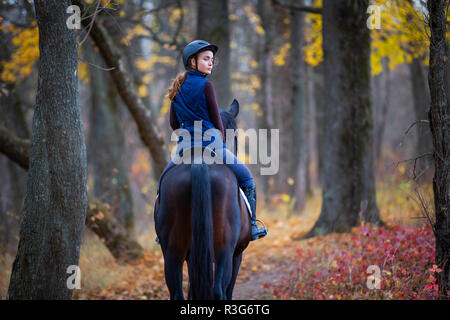 Ragazza adolescente di equitazione nel Parco d'autunno. Felice Cavaliere con il suo stallone a camminare Foto Stock