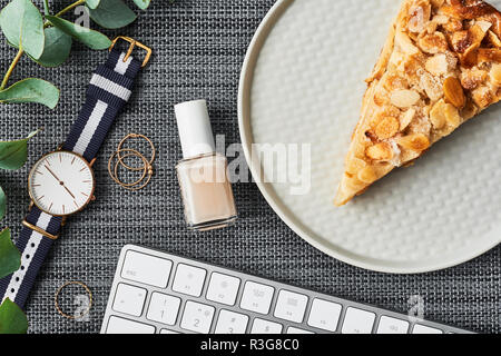 Accogliente business composizione con il bianco della tastiera del computer, smalto per unghie, anelli, impianto di eucalipto, donna guarda e torta di mele sulla piastra su backgroun grigio Foto Stock