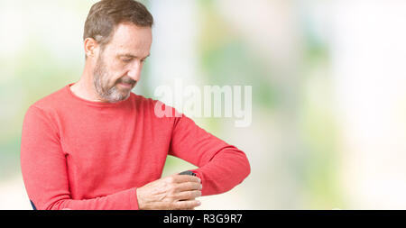 Bello medioevo annoso senior uomo che indossa un maglione invernale su sfondo isolato controllando il tempo su orologio da polso, rilassato e fiducioso Foto Stock