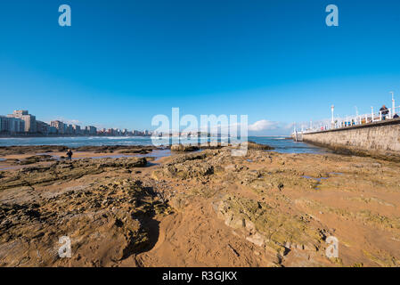 Gijon, Spagna - 19 Novembre 2018: Spiaggia di San Lorenzo e il turista a camminare su una passeggiata in una giornata di sole Foto Stock