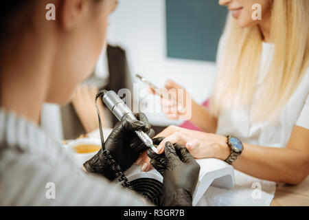 Bionda donna avente manicure fatto usando il suo smartphone Foto Stock