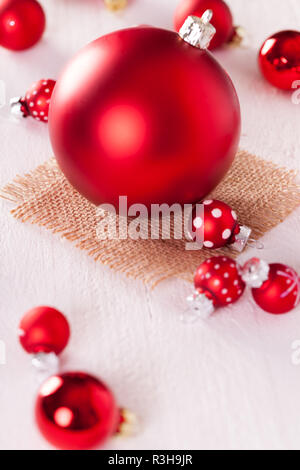 Grandi e piccoli baubles rosso su una tavola di legno con un sacco di iuta Foto Stock