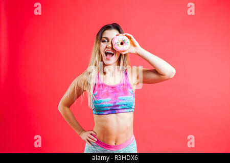 SPORTY affascinante ragazza in ultra-violetta con ciambelle isolato su rosso Foto Stock