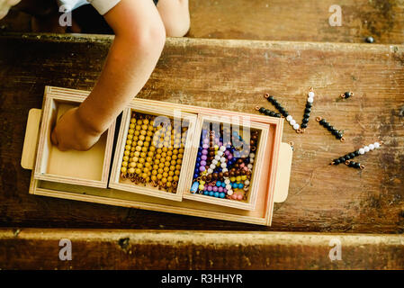 Le mani di un bambino la manipolazione di materiali didattici per imparare a contare in una classe Montessori. Foto Stock