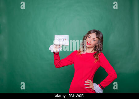 Pubblicità. Donna in abito rosso. Donna sorridente che mostra scheda con la parola amore e il cuore rosso su sfondo verde. amore messaggio di testo.Positivo emozioni umane faccia espressioni.Happy valentines il concetto di saluto Foto Stock