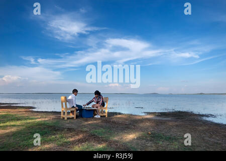 Due fratelli felici giocando una partita con gli scacchi vicino al lago nella natura Foto Stock