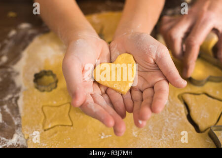 Close-up vista parziale del bambino tenendo a forma di cuore cookie crudi in mani Foto Stock