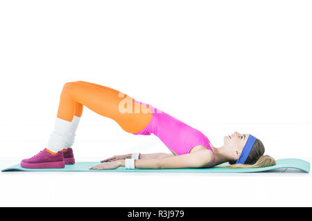 Vista laterale del sportivo sorridente ragazza distesa e formazione sul materassino yoga isolato su bianco Foto Stock
