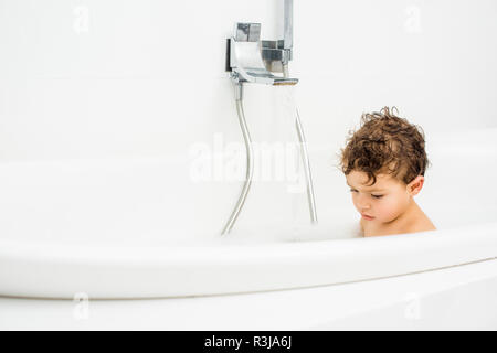 Il Toddler ragazzo seduto in bagno con acqua corrente Foto Stock