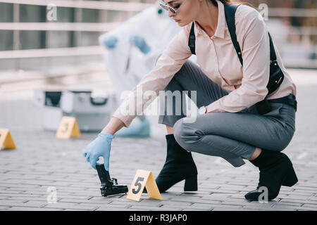 Detective femmina tenendo la pistola come un indizio con criminologo dietro alla scena del crimine Foto Stock