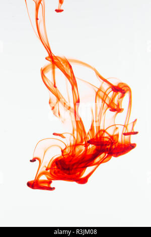 Colorante alimentare gocciolata in un bicchiere di acqua e disperdendo. Foto Stock