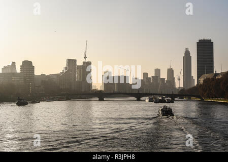 Lo skyline di Londra stagliano contro un tardo autunno bassa sera sun. Il fiume Tamigi del traffico fluviale. Costruzione di gru. Lambeth Bridge. Nine Elms. Costruzione Foto Stock