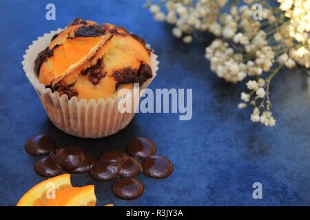 Arancione e muffin al cioccolato. Photo shot su piastrelle in ardesia con fiori come parte del sostegno in aggiunta con alcuni elementi di ingrediente del muffin Foto Stock