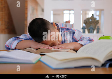 Lazy ha sottolineato giovane poco asian kid boy in appoggio di dormire sulla scrivania. bambino cadere addormentato. bambini stanchi di studiare in aula. infanzia formazione Foto Stock