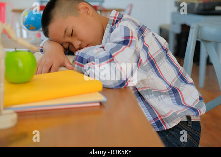 Lazy ha sottolineato giovane poco asian kid boy in appoggio di dormire sulla scrivania. bambino cadere addormentato. bambini stanchi di studiare in aula. infanzia formazione Foto Stock