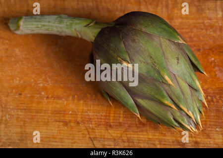 Carciofo crudo su un rustico tagliere di legno Foto Stock