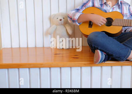 Asian kid bambino suonare la chitarra ukulele a casa. I bambini le attività per il tempo libero Foto Stock