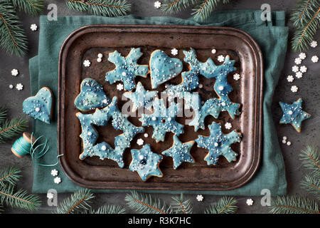 Vassoio di biscotti di Natale nelle forme di fiocchi di neve, stelle e sente di metallo sul vassoio da forno, piatto giaceva su sfondo scuro con ramoscelli di abete e cospargere di zucchero Foto Stock