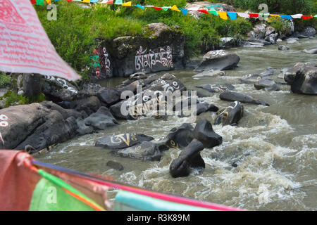 Rocce dipinte con parole di preghiera e la preghiera di bandiere nel fiume, Tagong, western Sichuan, Cina Foto Stock