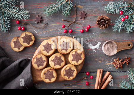 Biscotti di Natale con cioccolato stella con choco stelle, cannella e decorate Abete rami. Piatto sui laici scuri in legno rustico sfondo. Foto Stock