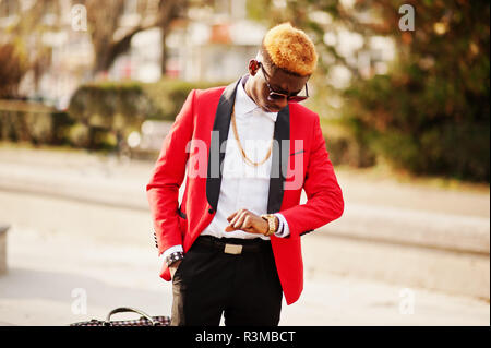 La moda americana africana modello uomo in tuta rossa, con in evidenza i capelli e la borsetta poste lungo la strada e guardando i suoi orologi. Foto Stock