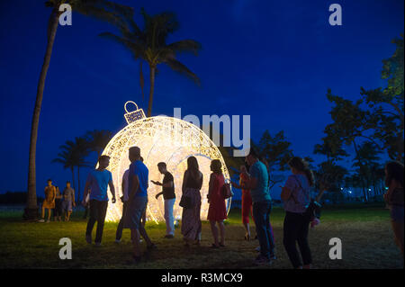 MIAMI - circa dicembre, 2017: i visitatori si radunano per scattare foto di fronte a un gigante illuminato ornamento di Natale impostato nelle palme di Lummus Park. Foto Stock