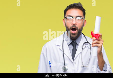 Adulto medico ispanica uomo grado di contenimento su sfondo isolato paura in stato di shock con una faccia a sorpresa, paura e eccitati con espressione di paura Foto Stock