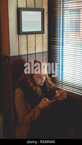 Donna che utilizza il cellulare mentre un caffè nella caffetteria Foto Stock