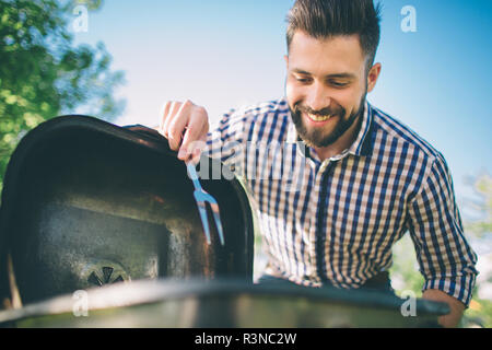 Uomo bello preparare il barbecue per gli amici. l uomo la cottura della carne sul barbecue - Chef mettendo alcuni salumi e salsiccia per pizza sul grill nel parco outdoor - Concep Foto Stock