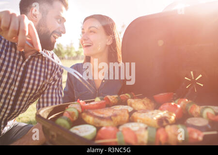 Amici fare barbecue e avente il pranzo nella natura. Giovane avendo divertimento mentre mangiando e bevendo in un pic-nic - le persone felici a barbecue party Foto Stock