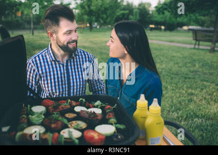 Amici fare barbecue e avente il pranzo nella natura. Giovane avendo divertimento mentre mangiando e bevendo in un pic-nic - le persone felici a barbecue party Foto Stock