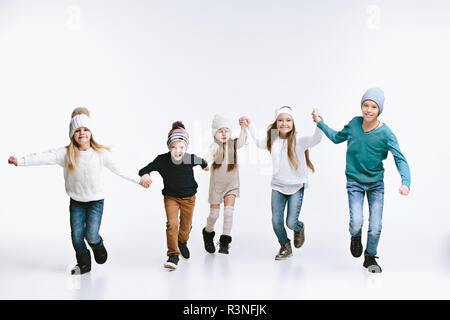 Un gruppo di bambini nella luminosa abbigliamento invernale, isolato su bianco studio. Moda, infanzia felice concetto emozioni Foto Stock