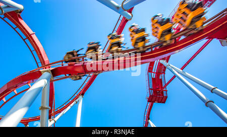 Giallo roller coaster con le persone all'interno di muoversi rapidamente e ad alta velocità, nel binario a rulli nel parco di divertimenti per il divertimento con cielo blu chiaro Foto Stock