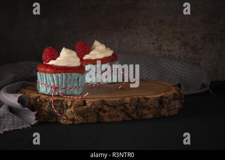 Tortini di rosso con la glassa di formaggio cremoso e lamponi scuro su un tavolo di legno. Foto Stock