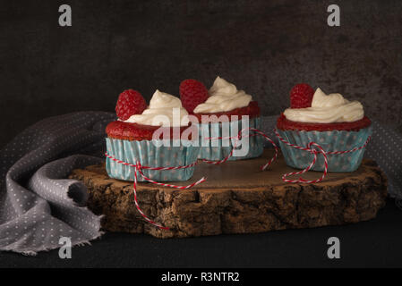 Tortini di rosso con la glassa di formaggio cremoso e lamponi scuro su un tavolo di legno. Foto Stock