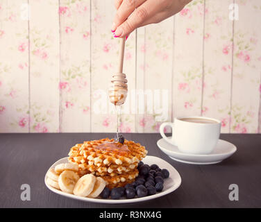 Donna versando del miele per deliziosi waffle sul tavolo di legno Foto Stock