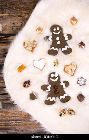 Gli uomini di panpepato e biscotti frollini a forma di stelle e cuori giacente insieme con golden baubles di natale su un bianco pelle d agnello. Fotografato da Foto Stock