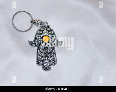 Un anello chiave nella forma di Fatima mano su un bianco sullo sfondo di seta. Simbolo di antico e di moderno e tradizionale souvenir turistici della Tunisia. Foto Stock
