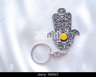 Un anello chiave nella forma di Fatima mano su un bianco sullo sfondo di seta. Simbolo di antico e di moderno e tradizionale souvenir turistici della Tunisia. Foto Stock