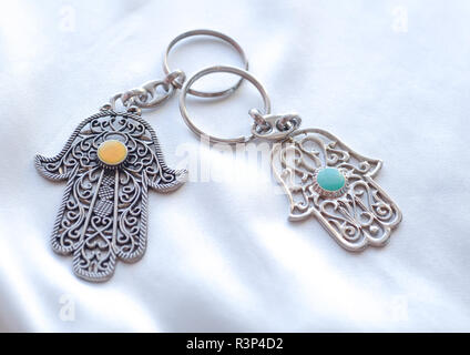 Due anelli di chiave a forma di mano di Fatima su un bianco sullo sfondo di seta. Simbolo di antico e di moderno e tradizionale souvenir turistici della Tunisia. Foto Stock