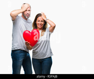 Medioevo ispanico casual giovane in amore azienda cuore rosso su sfondo isolato ha sottolineato con la mano sulla testa, sconvolto con vergogna e la sorpresa di fronte, Foto Stock