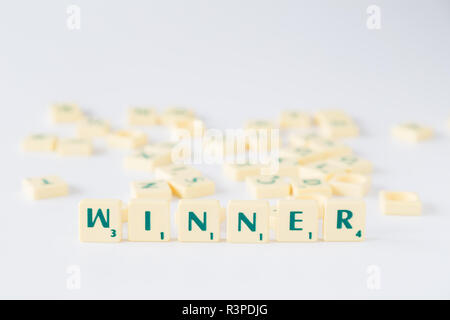 Focus sulla parola "vincitore" fatta di gioco SCRABBLE lettera di piastrelle con valore di punteggio, piastrelle casuale miscelato fino in background. Profondità di campo. Foto Stock
