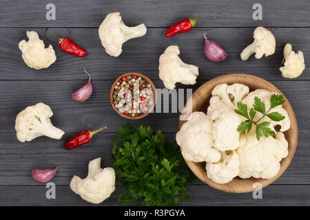 Cavolfiore fresco tagliato in piccoli pezzi in ciotola di legno con aglio e peperoncino nero su sfondo di legno Foto Stock