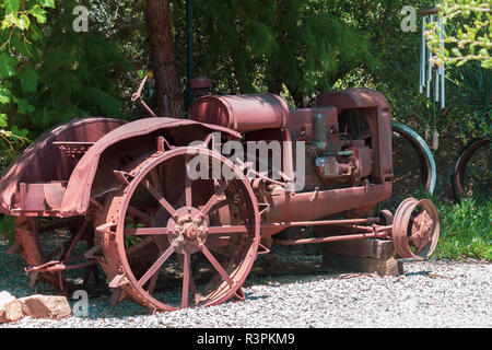 Depressione era arrugginito antichi ruota in acciaio trattore agricolo si è ritirato nel quadro di una shade tree Foto Stock