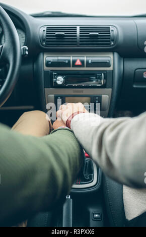 Donna mettendo la mano sulla mano d'uomo utilizzando la leva del cambio in auto Foto Stock