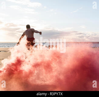 Uomo che fa del movimento di formazione presso la spiaggia con fumo di colore rosso Foto Stock