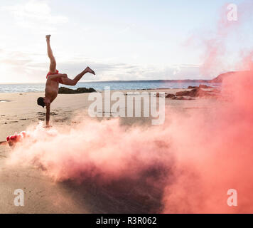 Uomo che fa del movimento di formazione presso la spiaggia con fumo di colore rosso Foto Stock