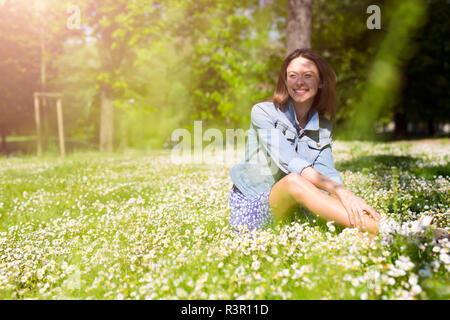 Sorridente giovane donna seduta in un parco Foto Stock