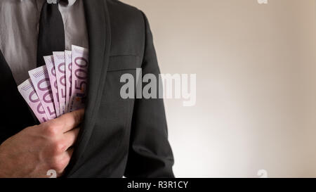 Vista frontale di imprenditore piazzando cinque cento Euro Bills nella tasca interna della sua tuta giacca. Concettuale del business la corruzione. Foto Stock