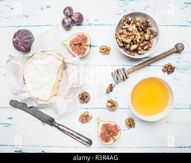 Formaggio Camembert sul vecchio tavolo in legno con una ciotola di noci, miele, un vintage coltello da tavola, tagliare i fichi e uva, vista dall'alto Foto Stock